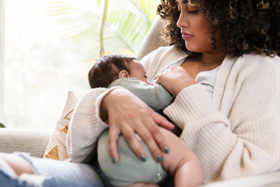 A person with curly hair is breastfeeding a baby while sitting on a couch. They seem relaxed and nurturing in a cozy environment