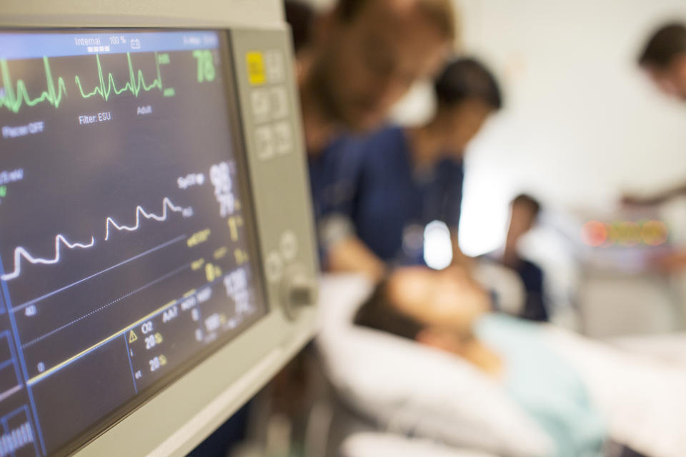 Healthcare workers tend to a patient in a hospital bed, with medical monitors displaying vital signs in the foreground