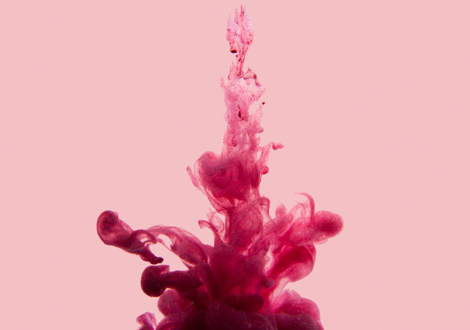 Pink ink swirls in water creating abstract and intricate shapes against a plain background