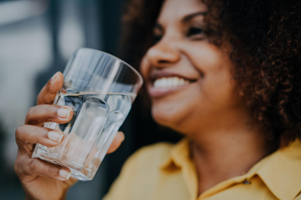 A person laughs while holding a glass of water close to his face