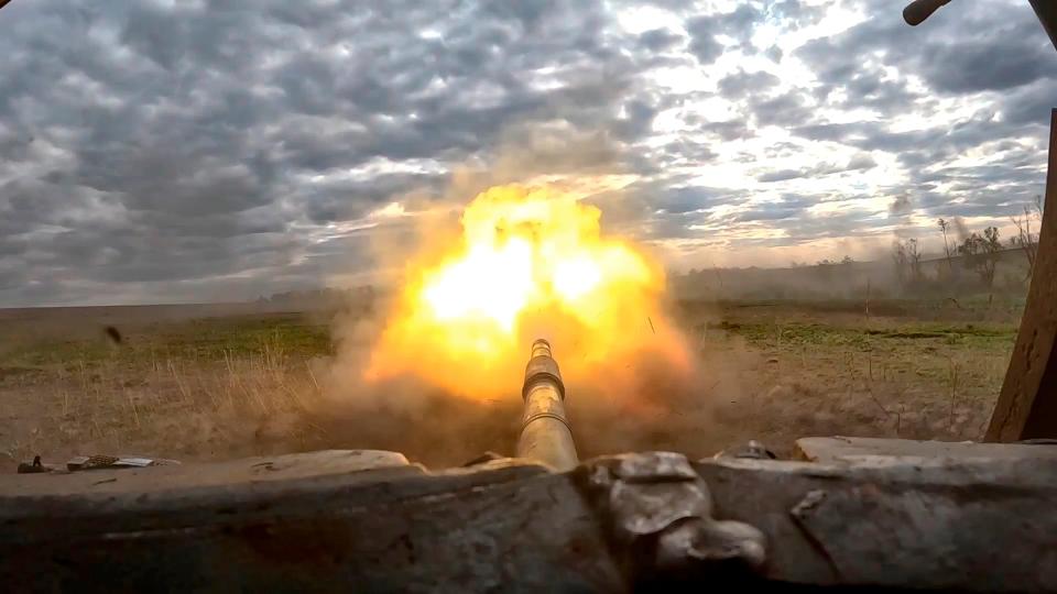 Fire erupts from the barrel of a T-90 tank on a devastated battlefield in Ukraine.