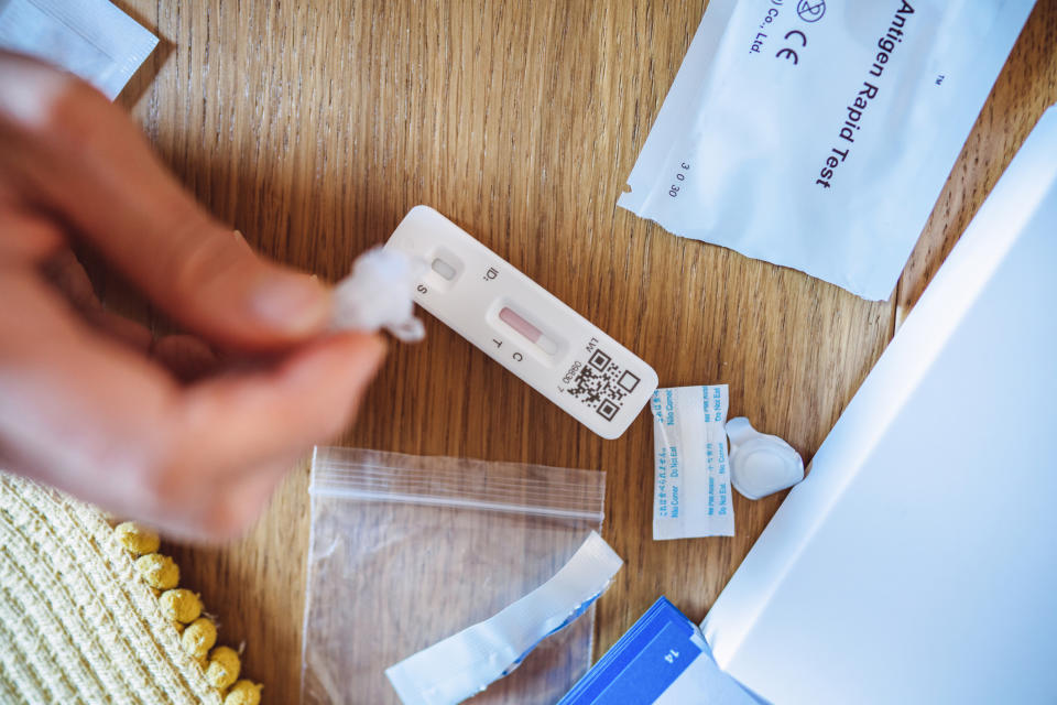 A person performs a rapid antigen test for COVID-19 at home on a wooden surface, surrounded by test components and instructions