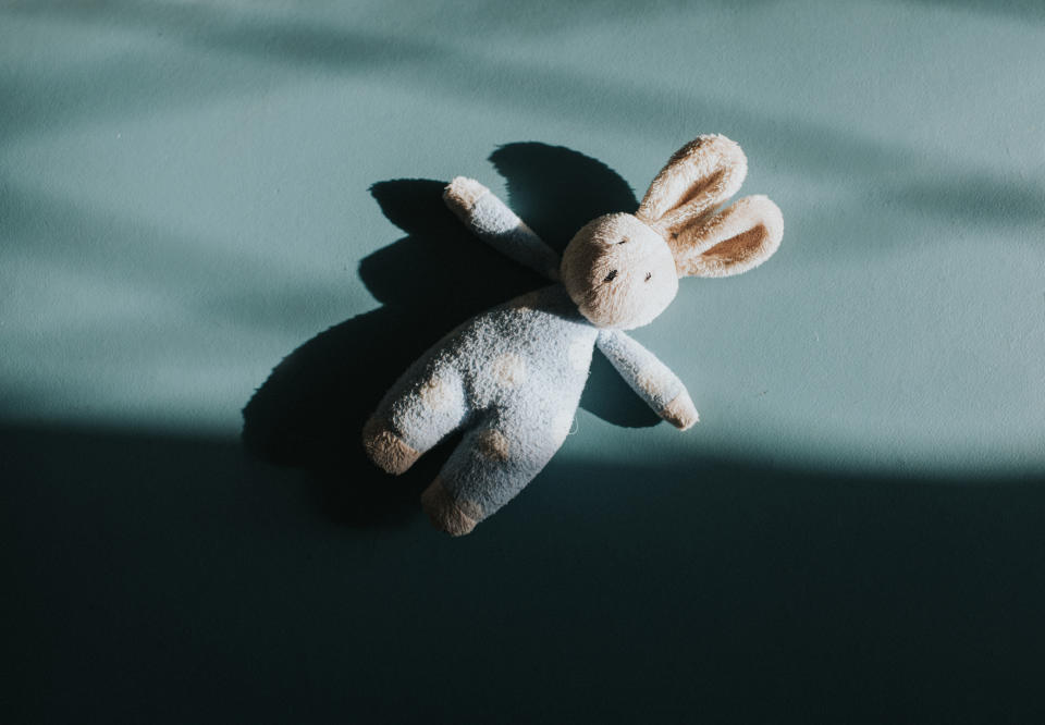 A plush rabbit toy lies on a flat surface, partially in the shade