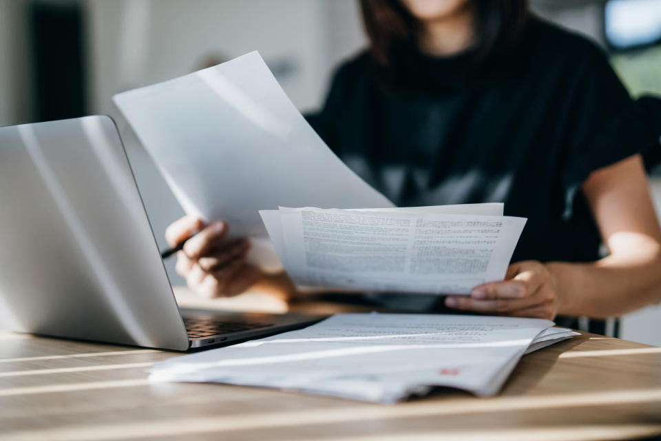 Person at a desk going through documents with an open laptop