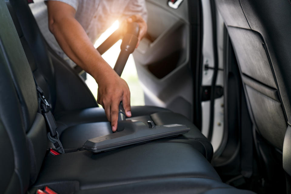 A person using a vacuum cleaner to clean the backseat of a car