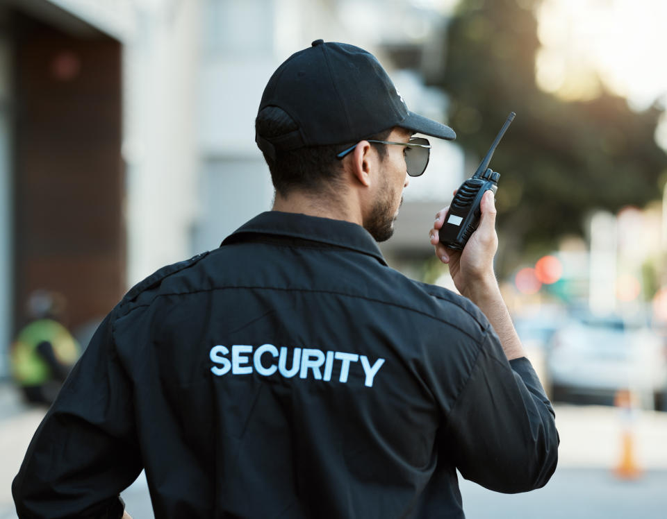 A uniformed security guard speaks into a walkie-talkie while off duty