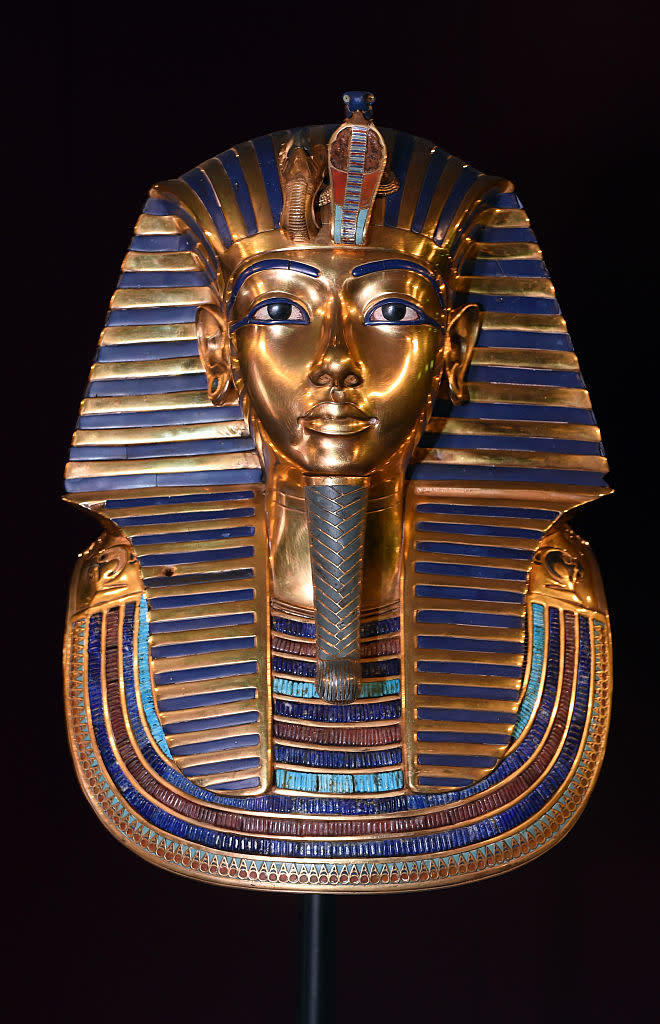 Golden burial mask of Egyptian Pharaoh Tutankhamun, decorated with intricate designs and semi-precious stones, displayed against a dark background