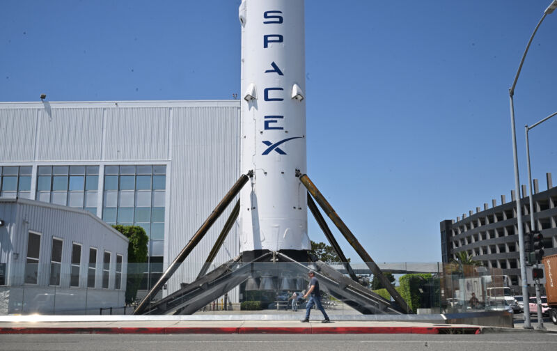 A pedestrian walks past a flying Falcon 9 booster at SpaceX's Hawthorne, California, headquarters on Tuesday, the same day Elon Musk announced he was moving the company's headquarters to Texas.