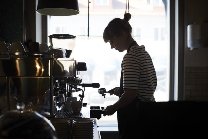 Een barista in een gestreept shirt bedient een espressomachine in een café