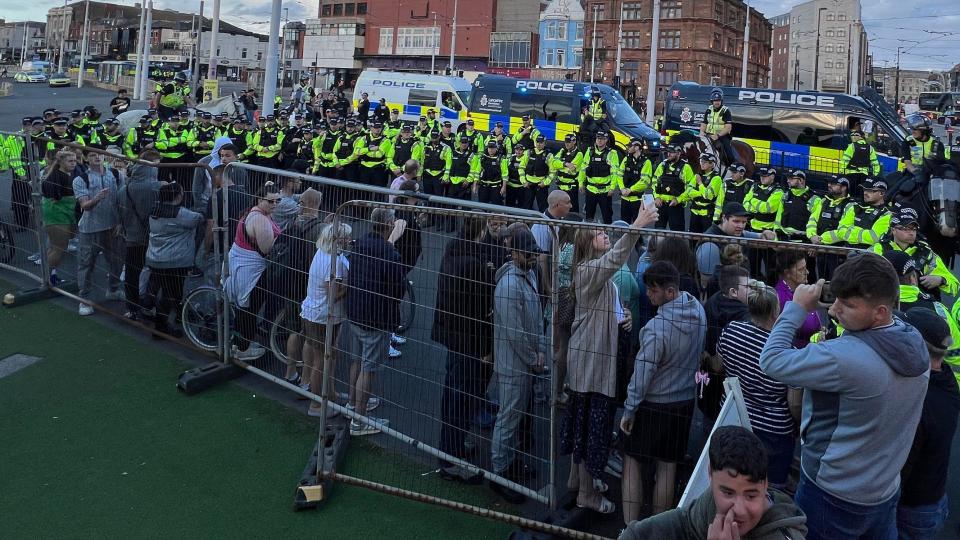 A group of protesters stand along a fence after being surrounded by a line of police officers in high-visibility vests