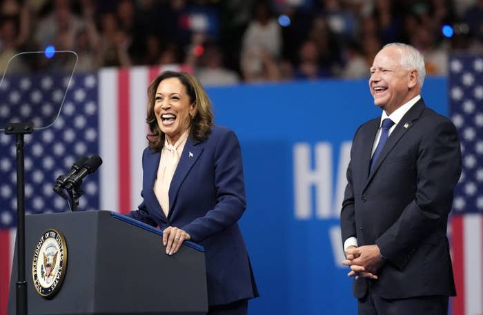 Kamala Harris speaks at a podium wearing a vice presidential seal, smiling, while standing next to Minnesota Gov. Tim Walz, who is also smiling