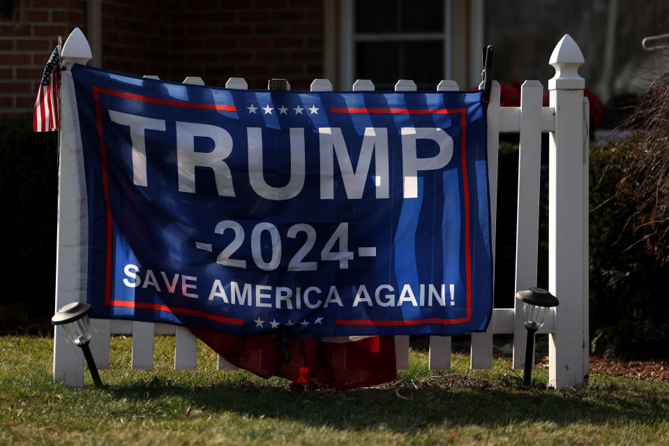 A banner with the text hangs on a white fence "TRUMP 2024 SAVE AMERICA AGAIN!"