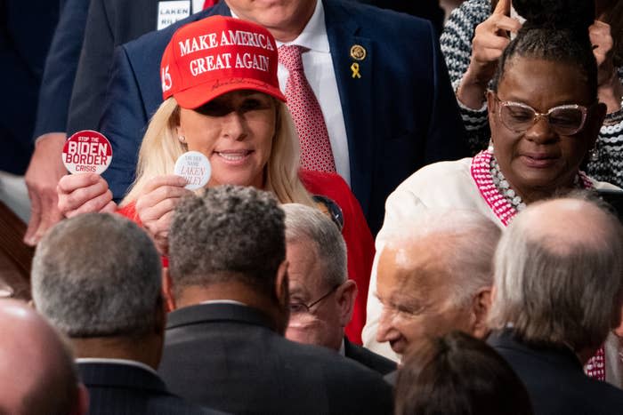 Kellyanne Conway, in a "Make America Great Again" hat, holding up buttons related to Biden's border crisis. She is surrounded by other people