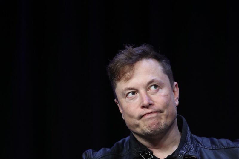 Elon Musk frowns as he sits on stage during an interview at a conference.