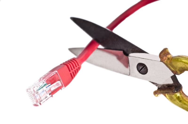 A pair of scissors cuts an Ethernet cable.