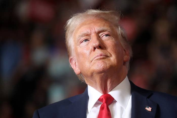 Donald Trump in suit and red tie, looking slightly upwards, in a public setting