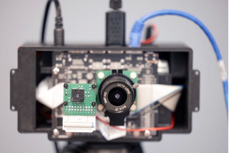 The front of a camera has been removed, revealing the internal components. A series of black and blue wires lead to the camera's connectors.