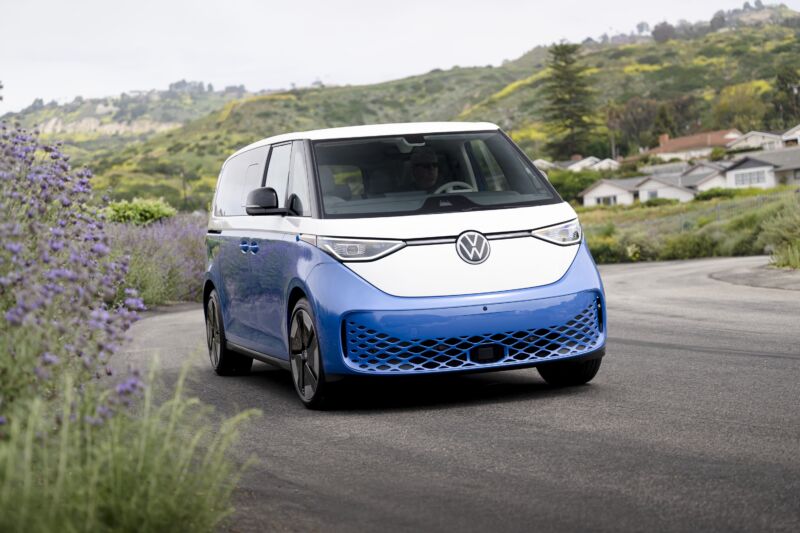 A white and blue VW ID Buzz drives on a road