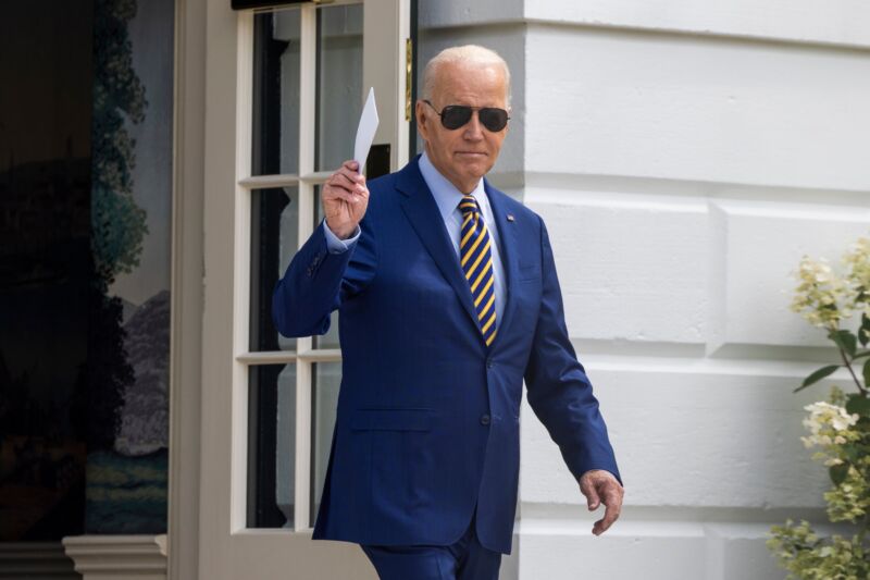 Joe Biden walks outside the White House, wearing sunglasses and holding a stack of index cards in his right hand.