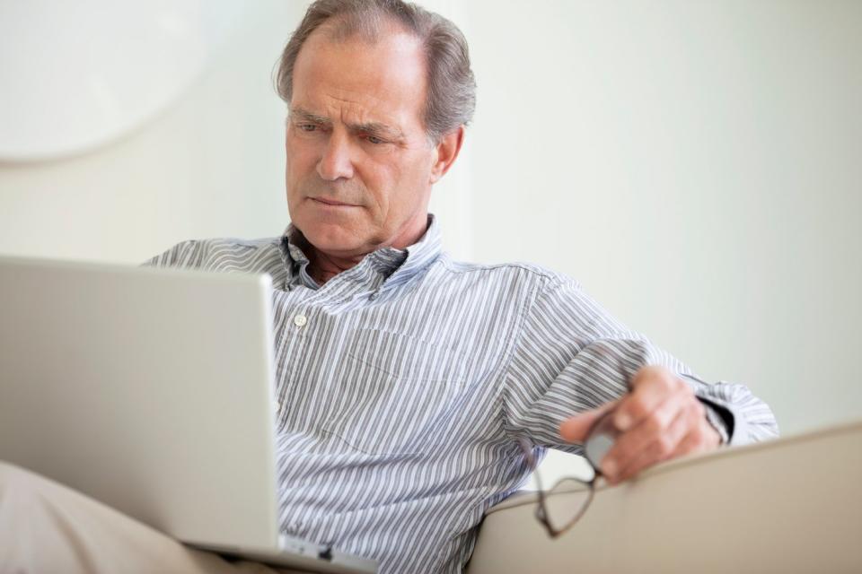 A person sitting on a couch critically reads the contents of an open laptop on his lap.