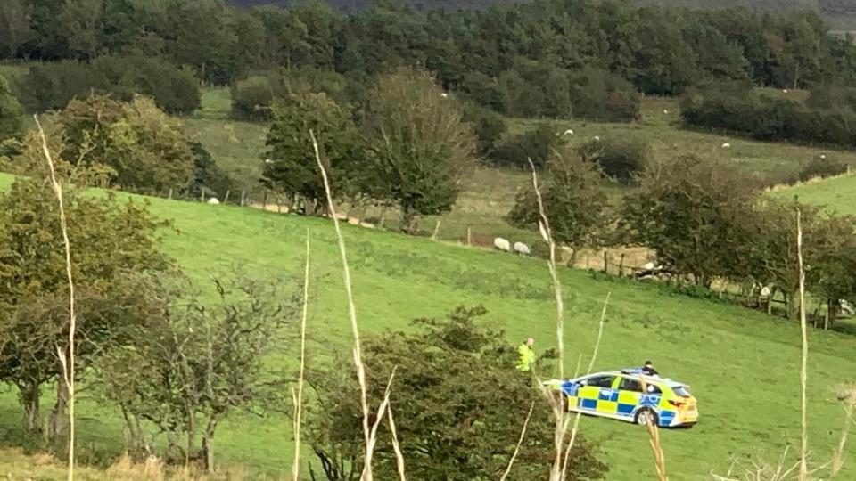 A police car and two officers in a field near Warcop in Cumbria, where the child was injured