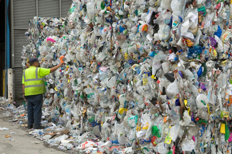 A man stands next to stacks of compressed plastic bottles.