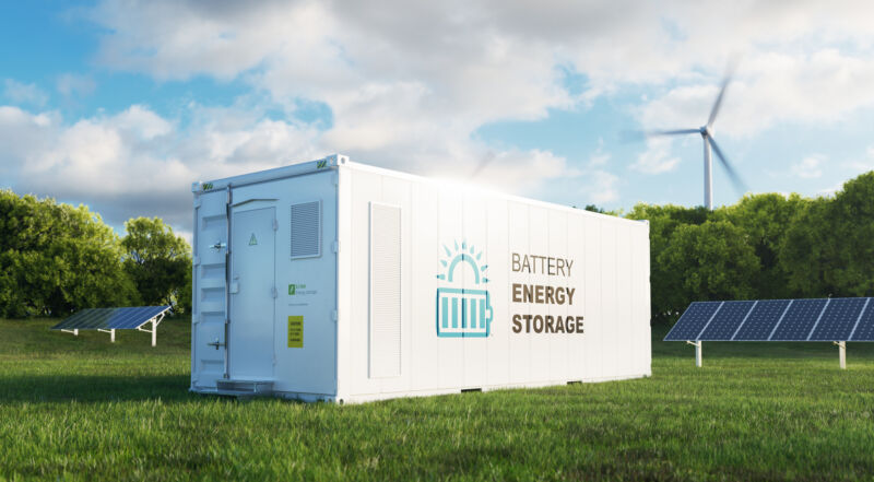 A shipping container with the battery symbol, among wind turbines and solar panels.