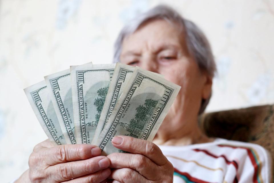 A person sits in a chair and counts a stack of hundred dollar bills in his hands. 