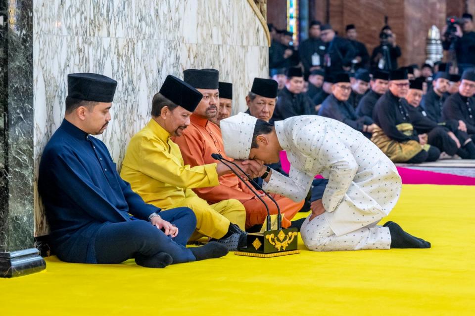 This handout photo taken by the Brunei Information Department on January 11, 2024 and released on January 12, 2024, shows Brunei's Prince Abdul Mateen, right, touching his forehead to the hand of his father, Brunei's Sultan Haji Hassanal Bolkiah, second from left, after his ceremony at the Sultan Omar Ali Saifuddien Mosque in Bandar Seri Begawan, Brunei (via AP)