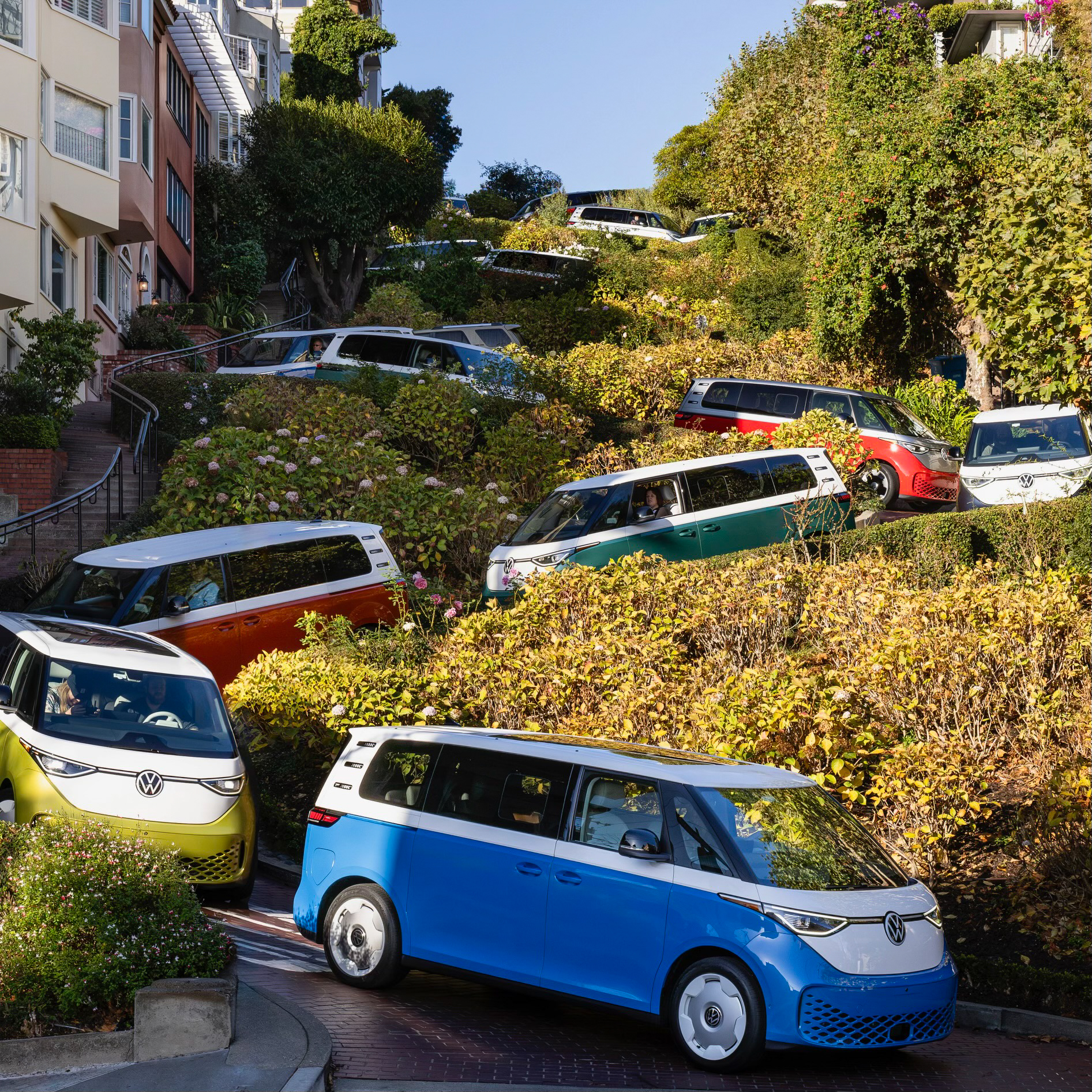 A convoy of brightly colored VW ID Buzzes drives down Lombard Street in San Francisco.