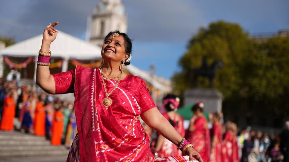 A woman in a pink and white sari looks at the sky as she dances at the event