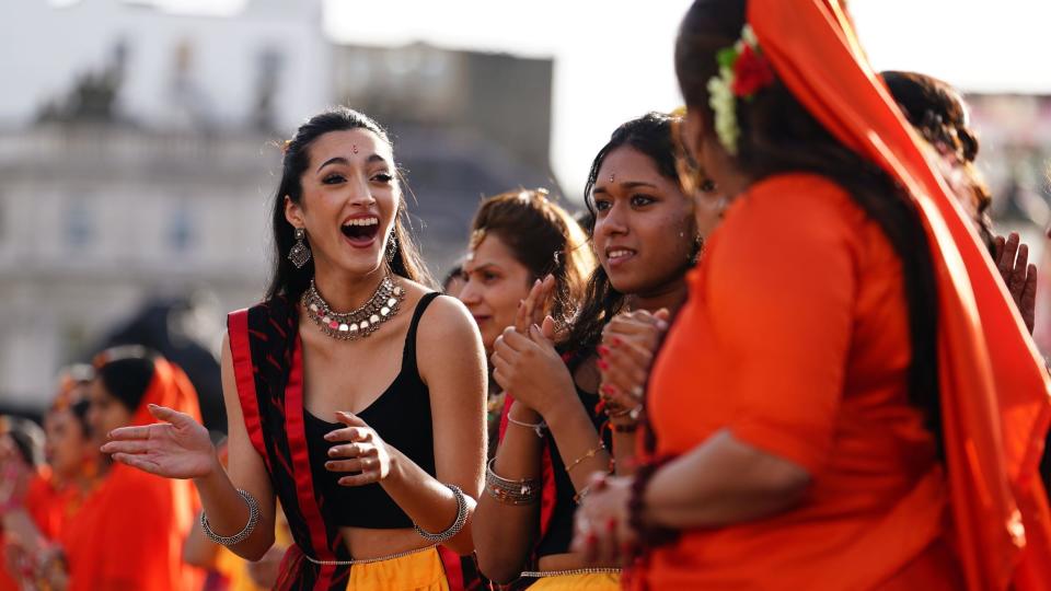 Female performers in black and orange clothing clap and chat in Trafalgar Square