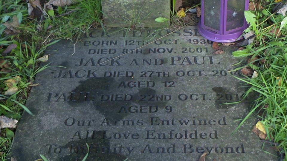 A gray headstone, engraved with dark gray letters, reading: Jack and Paul. Jack died on October 27, 2014, at the age of 12. Paul died on October 22, 2014, at the age of 9. Our arms entwined, all love enveloped to infinity and beyond.