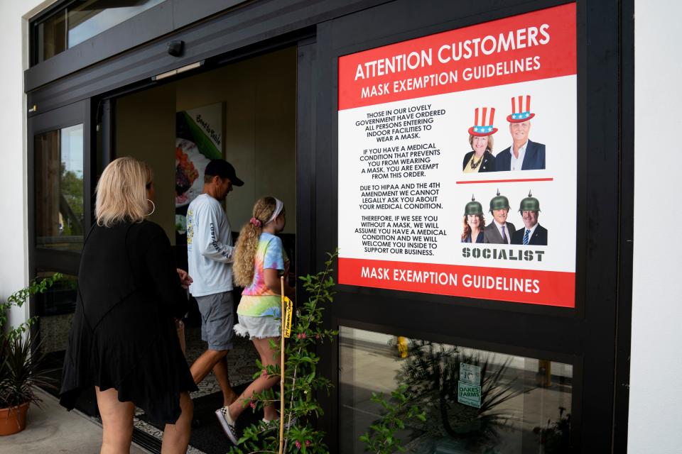 A sign with Seed to Table's mask exception guidelines hangs outside the store entrance during a rally in opposition to the mask mandate passed by the Collier County Commissioners on Tuesday, at Oakes Farms Seed to Table Market on Saturday, July 25, 2020. Collier County Commissioners who voted against the mandate are depicted wearing Uncle Sam hats, while those who voted for the mandate are depicted above the word Socialist.