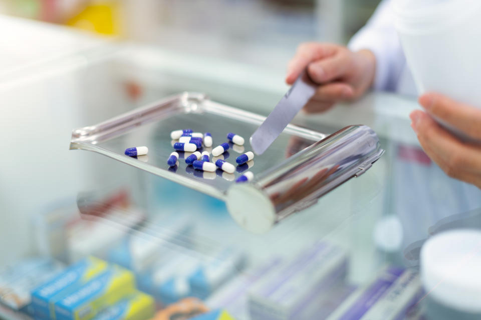 Pharmacist counting medicine capsules on a tray in a pharmacy environment