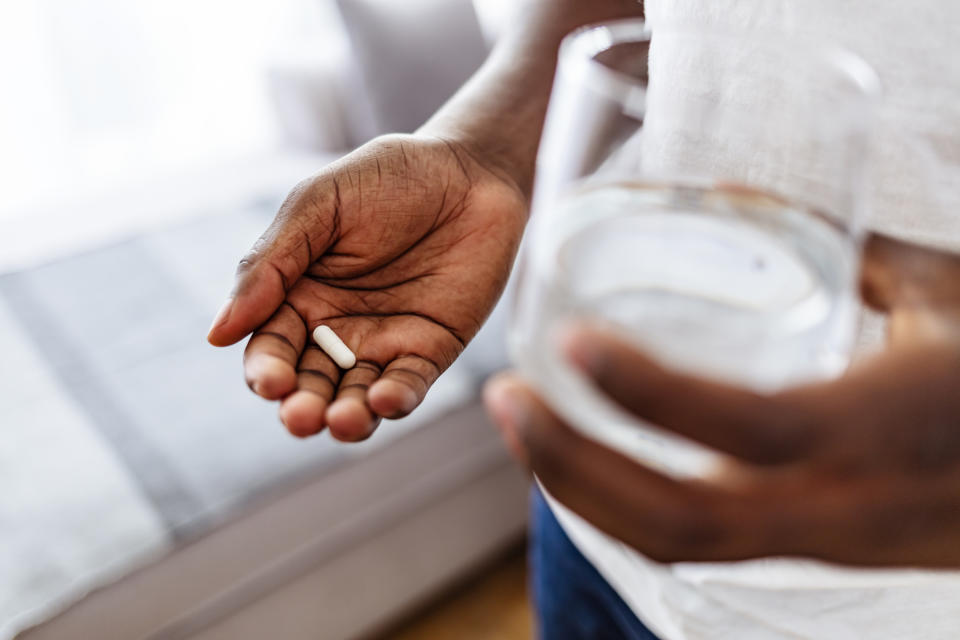 Person holding a pill in one hand and a glass of water in the other hand preparing to take medicine