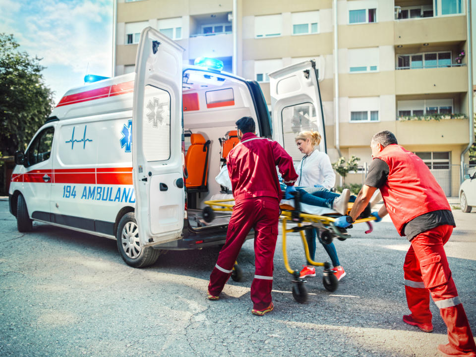 Paramedics assist a person on a stretcher in an ambulance parked outside an apartment building