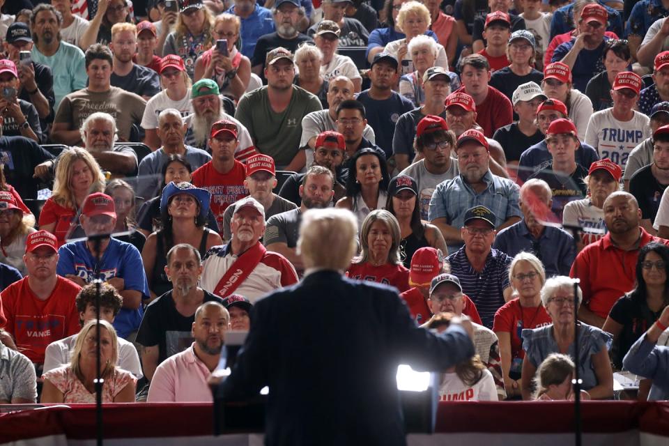 A man in a dark suit is seen facing a large crowd of people all looking ahead.