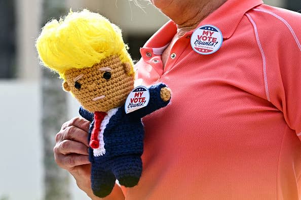 Person holding a crochet figure with styled hair and a suit. Both carry reading pins "My vote counts!"