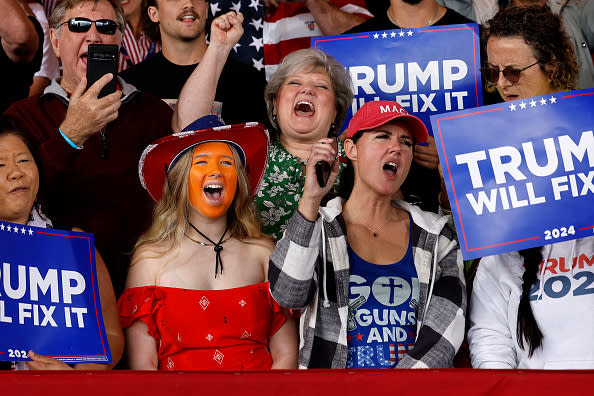 People at a meeting holding signs that say: "Trump will fix it in 2024," some wore clothing with a patriotic theme