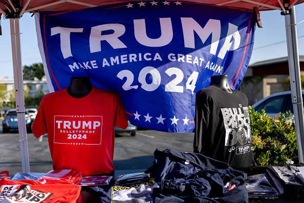 T-shirts and banners promoting Trump 2024 are displayed on mannequins and a table under a tent