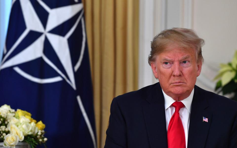 Mr Trump sits in front of a NATO flag in 2019