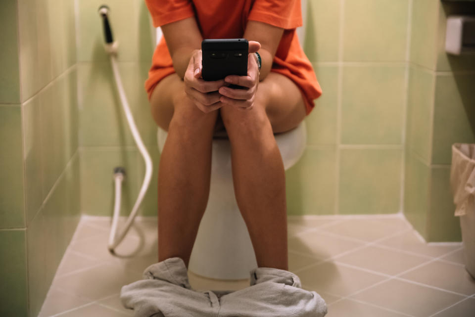 Person on toilet with smartphone, clothes on the ankles