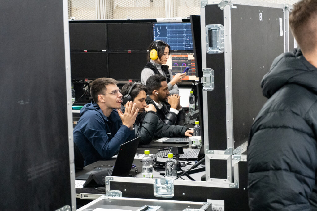 A group of engineers watch monitors in a race track garage.