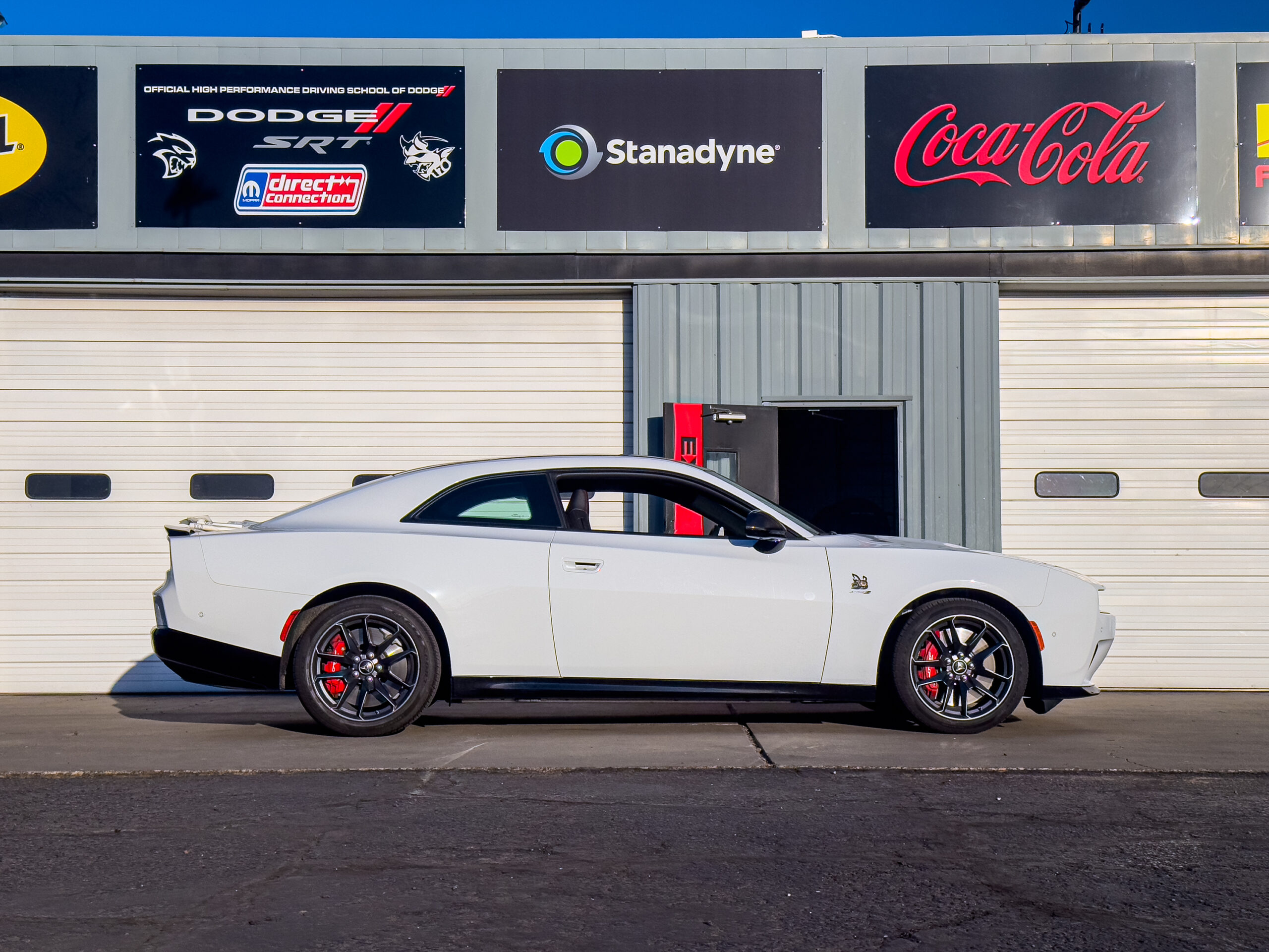 A white Dodge Charger Daytona, seen in profile against some garages on a race track