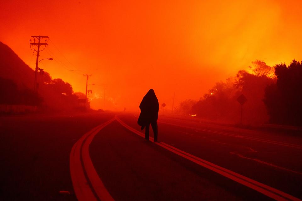 A person walks along Malibu Canyon road Tuesday as the Franklin Fire approaches in Malibu, California. The fire moved south Tuesday morning ((AP Photo/Eric Thayer))