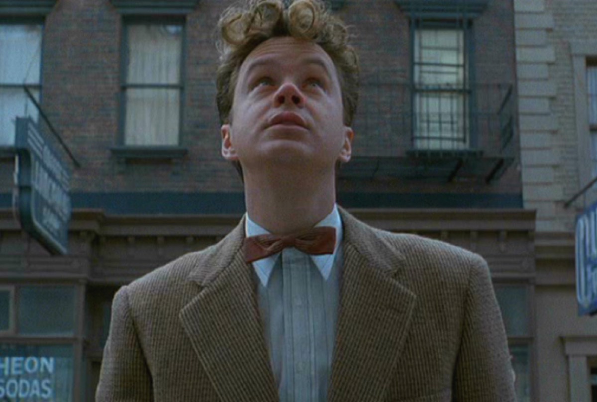 young man in 1950s suit looks up at a tall building