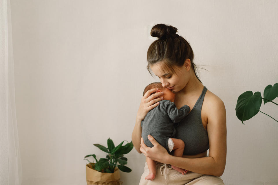 Woman gently holding a baby to her chest, sitting next to a plant in a serene setting