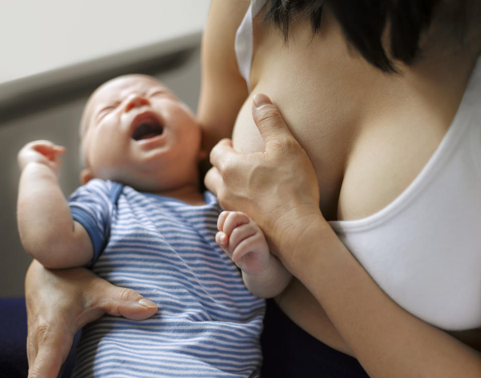 Person breastfeeding a baby wearing a striped outfit; the baby cries