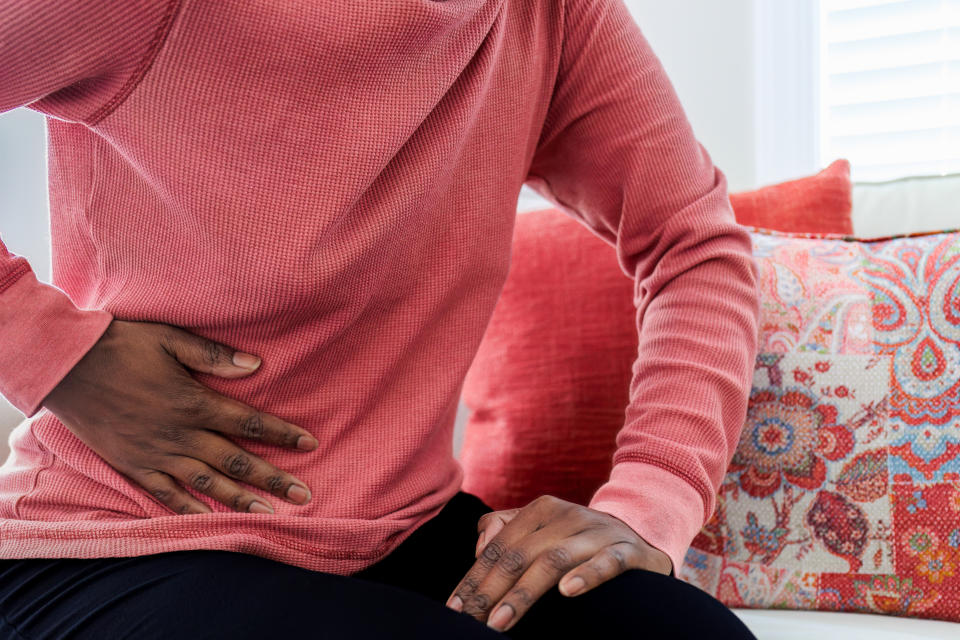 Person sits on sofa, holding stomach uncomfortably, next to decorative pillows